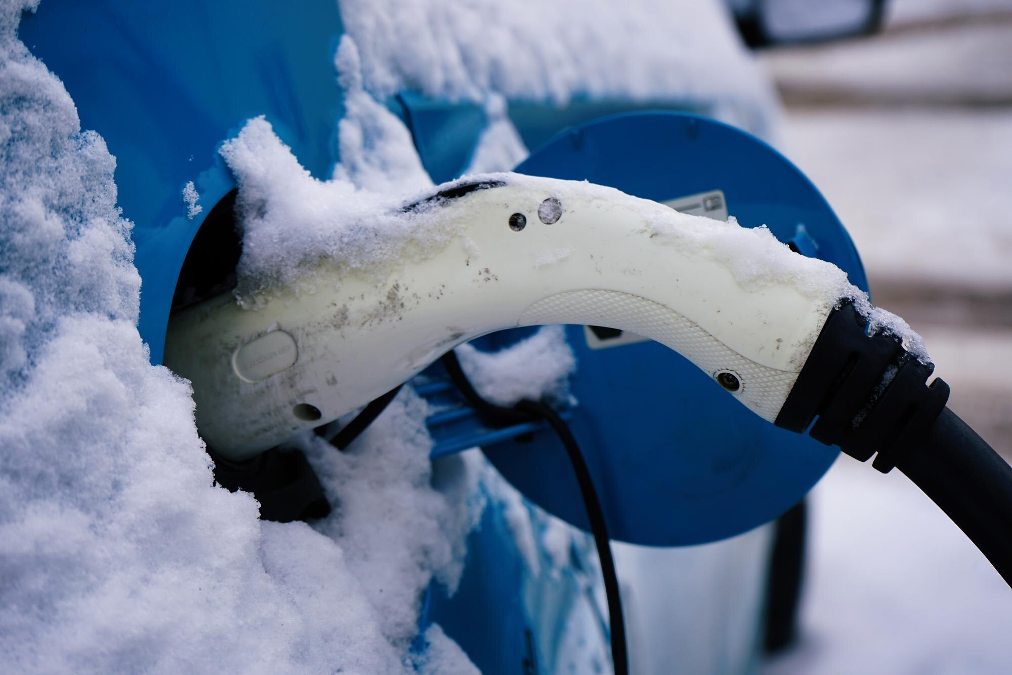 Esilämmitetty sähköauto latauksessa lumisella pysäköintialueella.
